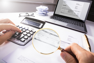 Person using a magnifying glass to review financial documents