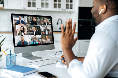 Man in office engaged in a remote work video meeting, with colleagues visible on his computer screen
