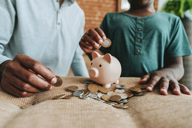Adult and child putting coins into a piggy bank