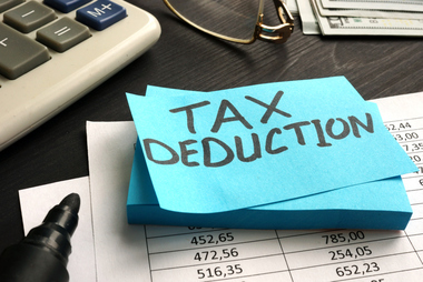 Calculator and spreadsheet on a desk with a blue sticky note reading “Tax Deduction.”