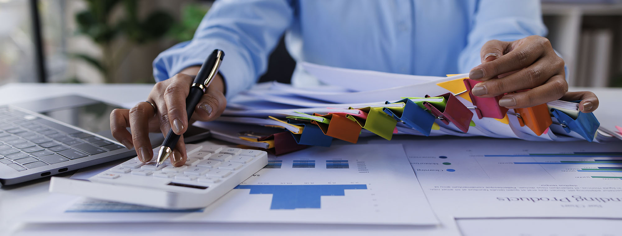 Person organizing papers and doing finance work on calculator and computer